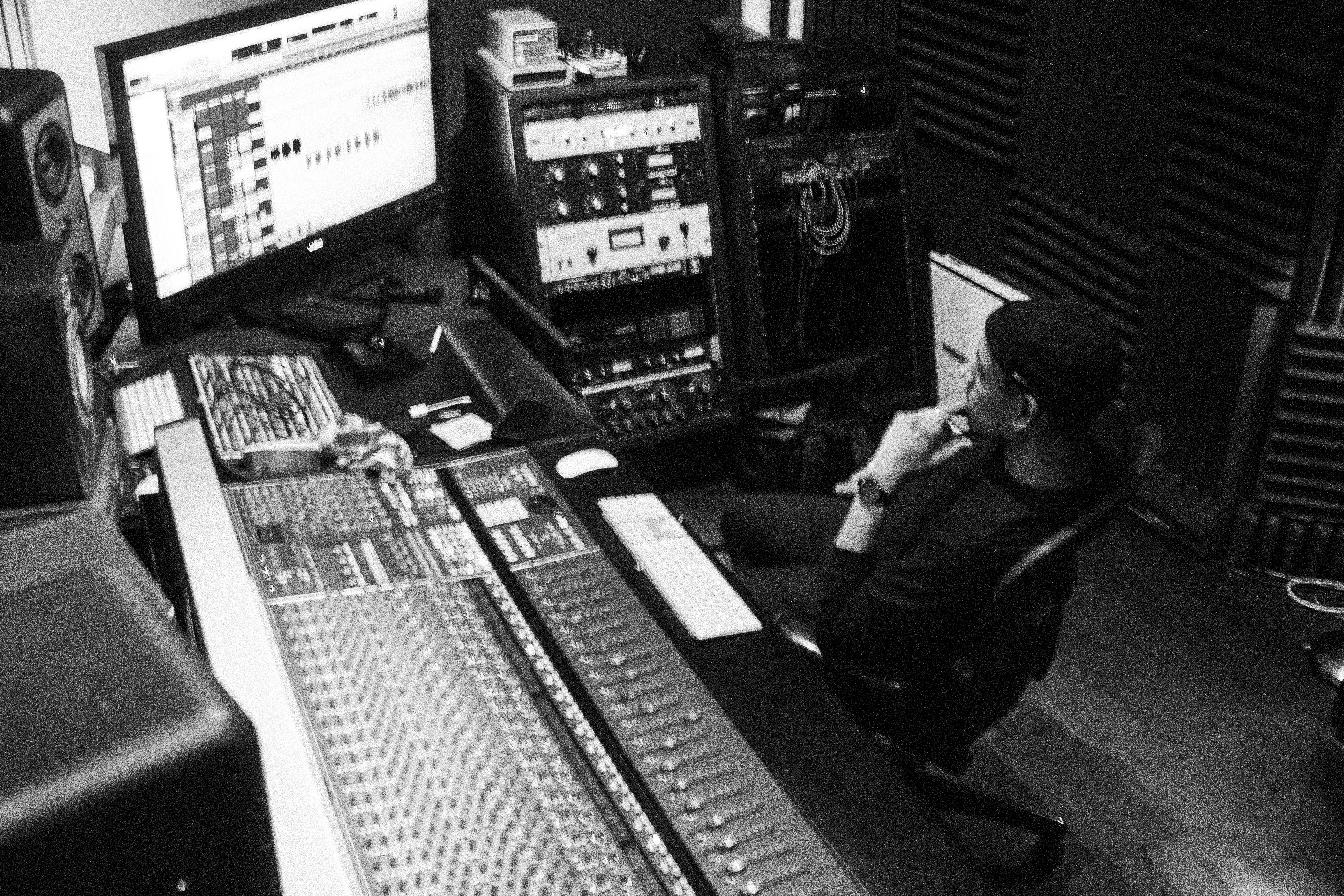 Maxim listening at a mixing console in a black-and-white studio photograph